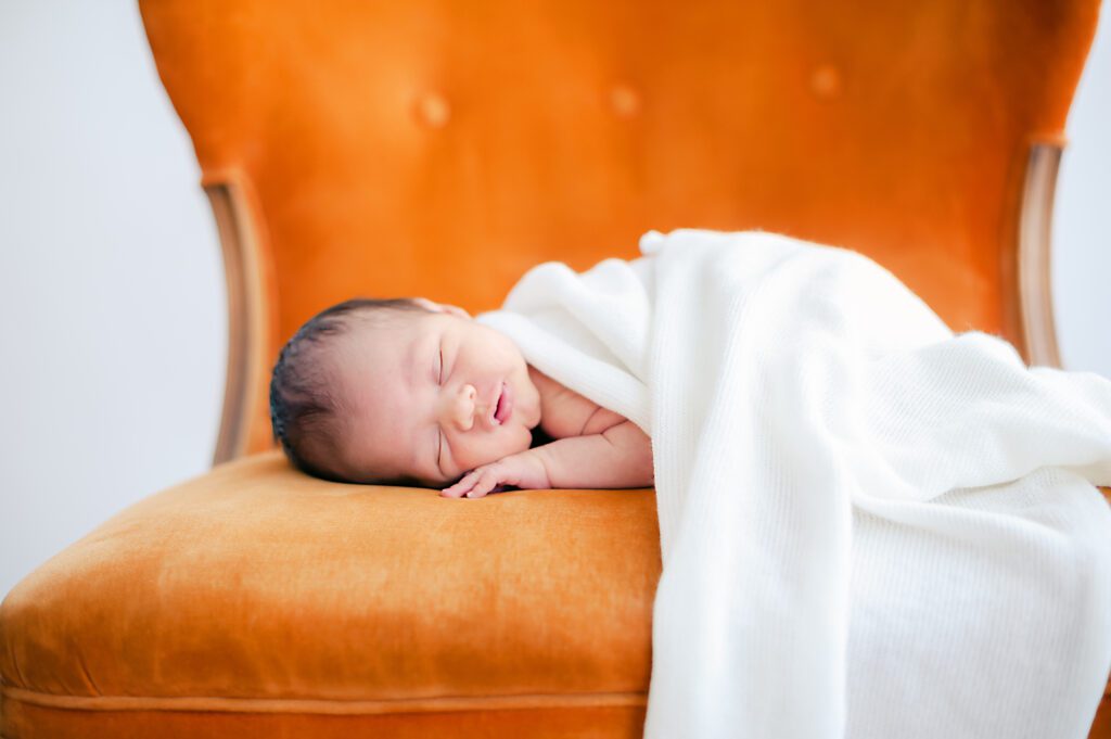 newborn baby boy sleeping on orange chair