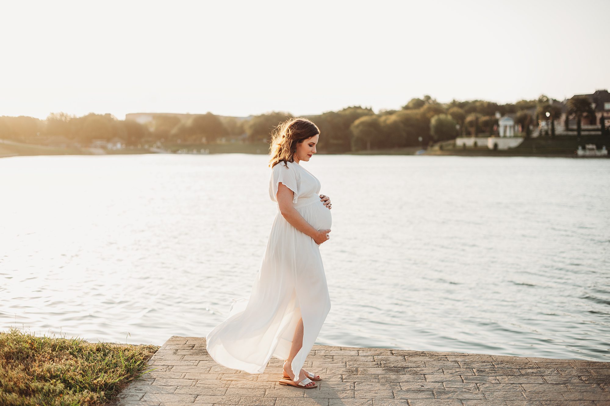 Pregnant woman standing lakeside holding her belly in a Dallas maternity photography session by Splendor Photography