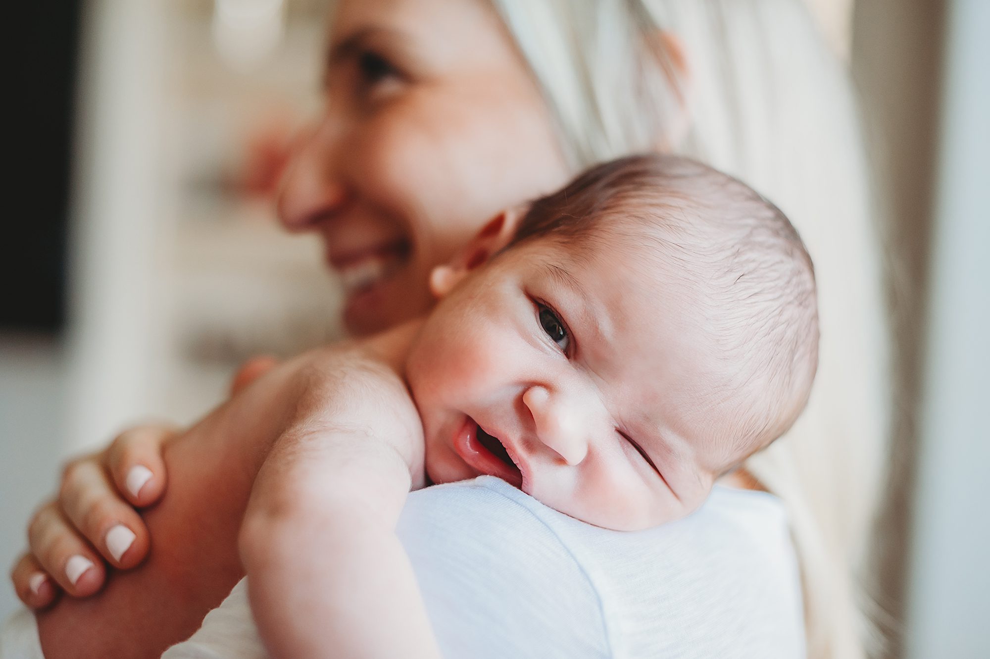 A newborn baby boy rest his head on his moms shoulder while looking at the camera in a Dallas lifestyle Newborn Photography session by Splendor Photography