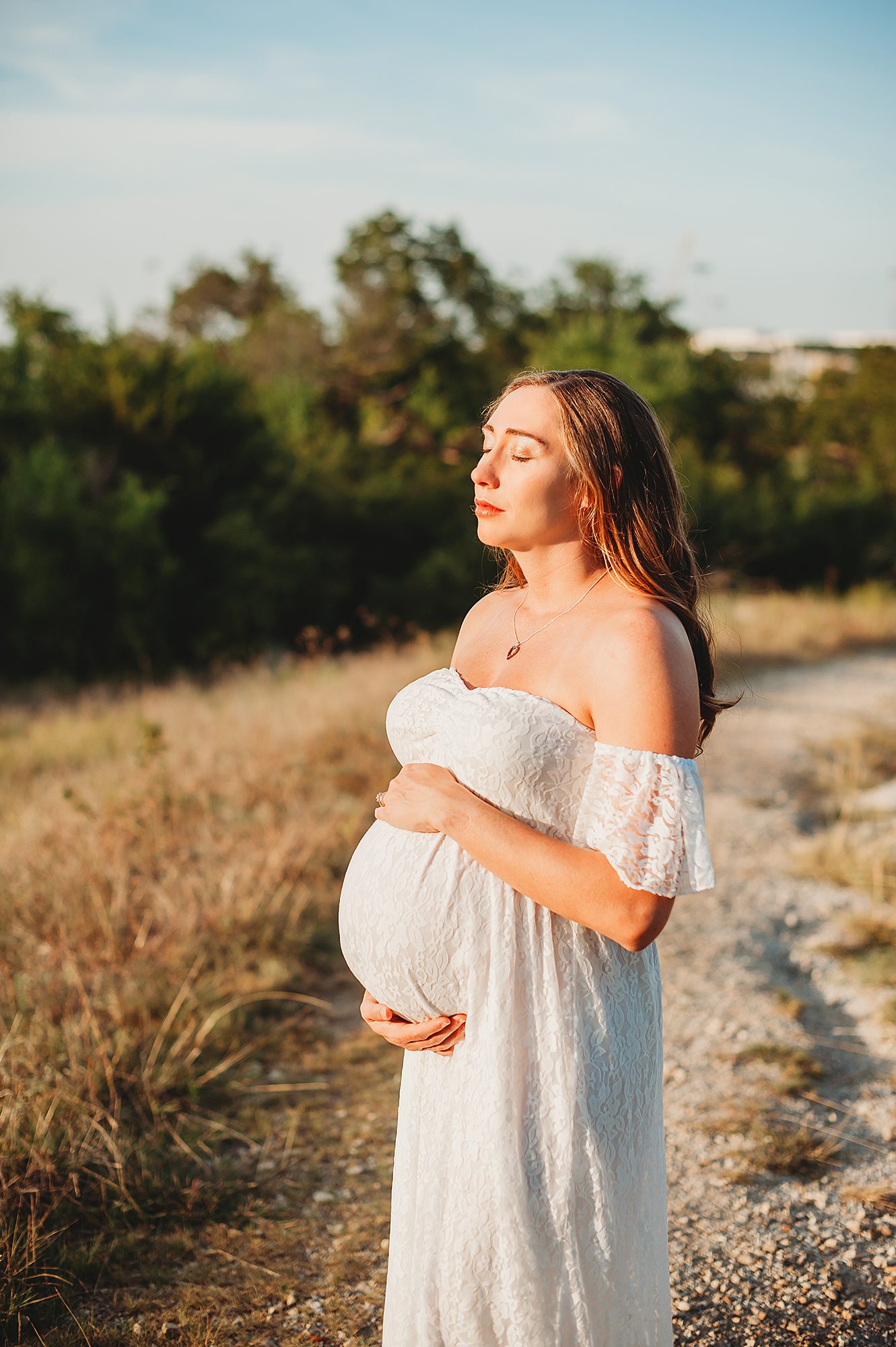 Pregnant Woman standing holding her belly facing the sun with her eyes closed in a Fort Worth Maternity Session by Splendor Photography